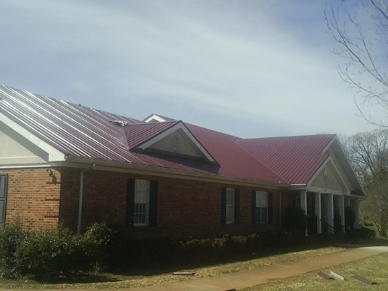 Red metal roof with gabled entries on a long brick building, from a Hail Damage Roof Repair job in Burns