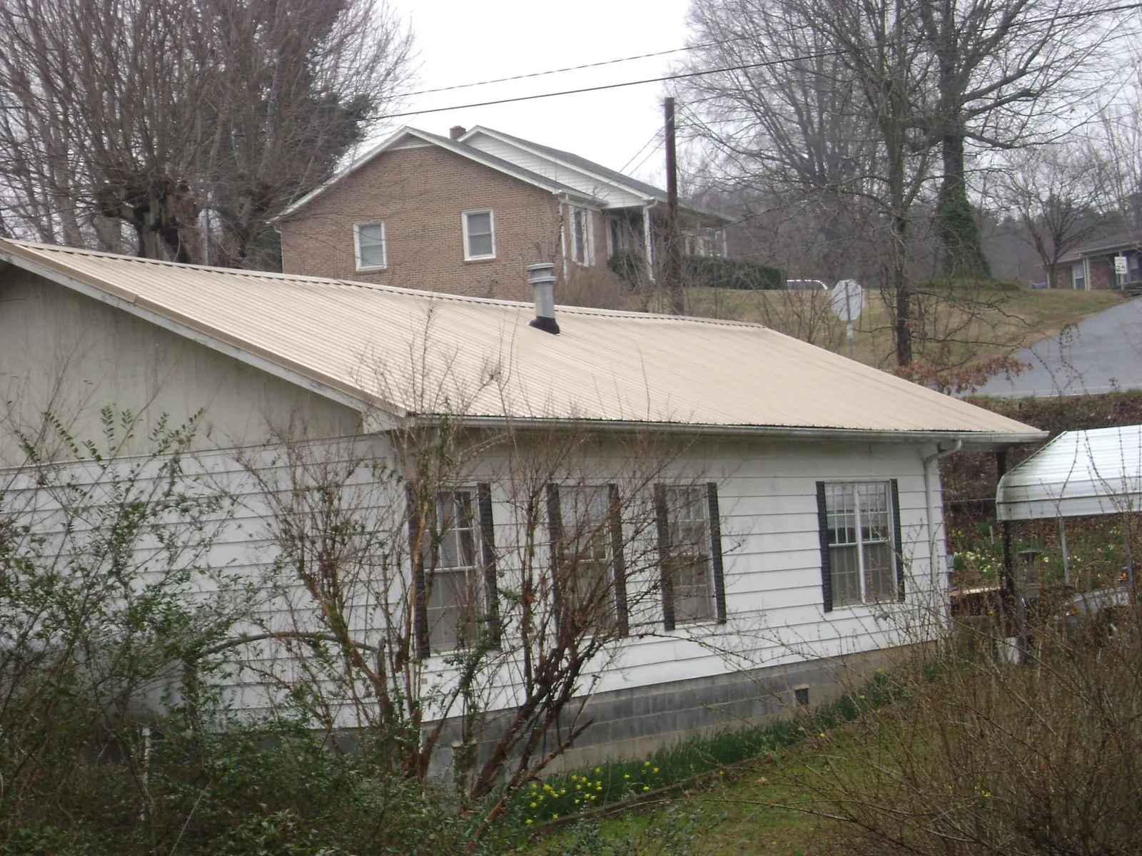 Tan metal roof on a white sided house set into a hillside — Commercial Roofing by Roofing Brothers in Burns