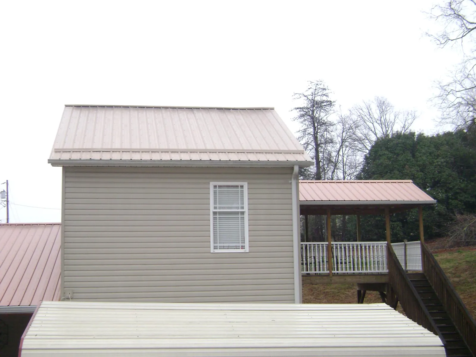 Tan metal roofs on a two story addition and attached porch, from a Roof Replacement job in Burns